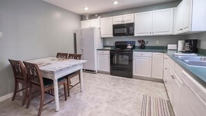 A kitchen with white cabinets, a refrigerator, stove, microwave, and a dining table with chairs. - Armory Quarters B (Bolivar)