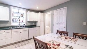 A kitchen with white cabinets, a window with shelves, and a dining table with placemats. - Armory Quarters B (Bolivar)