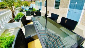 A patio with a glass table, black wicker chairs, and a colorful striped umbrella. - Cozy 2 Bedroom Flat W Pool/ Free Parking (Philipsburg)