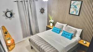 A modern bedroom with a bed, bedside tables, a mirror, curtains, and a wall-mounted picture. - Cozy 2 Bedroom Flat W Pool/ Free Parking (Philipsburg)
