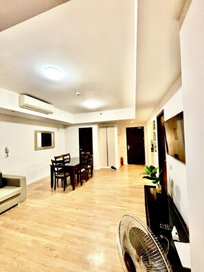 A spacious living area with a dining table, chairs, a sofa, a TV, and a fan. - Condo In Abreeza  Family and Spacious (Davao City)
