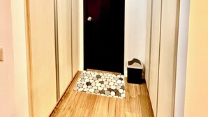 Un couloir étroit avec un plancher en bois, une porte noire et une petite marche menant à un espace carrelé.