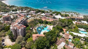 Vista aérea de un resort costero con piscina central, villas frente a la playa y una playa.