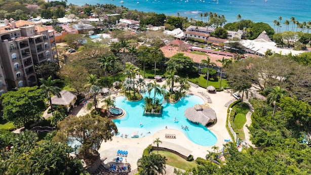 Un resort con una amplia piscina, palmeras y vista al océano.