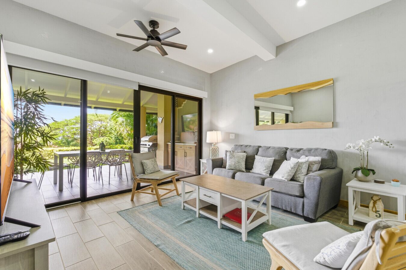 Sala de estar moderna com sofá, mesa de centro e área de jantar com cadeiras. Há uma porta de vidro deslizante que dá para uma varanda com móveis de exterior.
