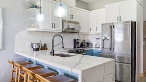 Una cocina moderna con armarios blancos, un refrigerador de acero inoxidable, una encimera de mármol y taburetes de madera.
