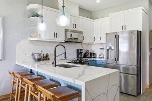A modern kitchen with white cabinets, a stainless steel refrigerator, a marble countertop, and wooden bar stools. - Two bedroom  in Costa Rica, Tamarindo (Tamarindo)