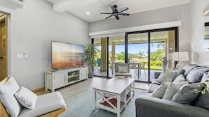 Amplia sala de estar con televisor de pantalla plana, ventilador de techo y un gran ventanal corredero que da a un patio con mobiliario exterior.