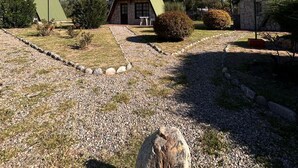 Une rangée de cabanes aux toits triangulaires et aux murs de pierre, entourées de chemins de gravier et de quelques touffes d’herbe, sous un ciel bleu dégagé.