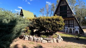 Une cabane avec une façade en pierre, un toit végétalisé et une petite terrasse avec des chaises.