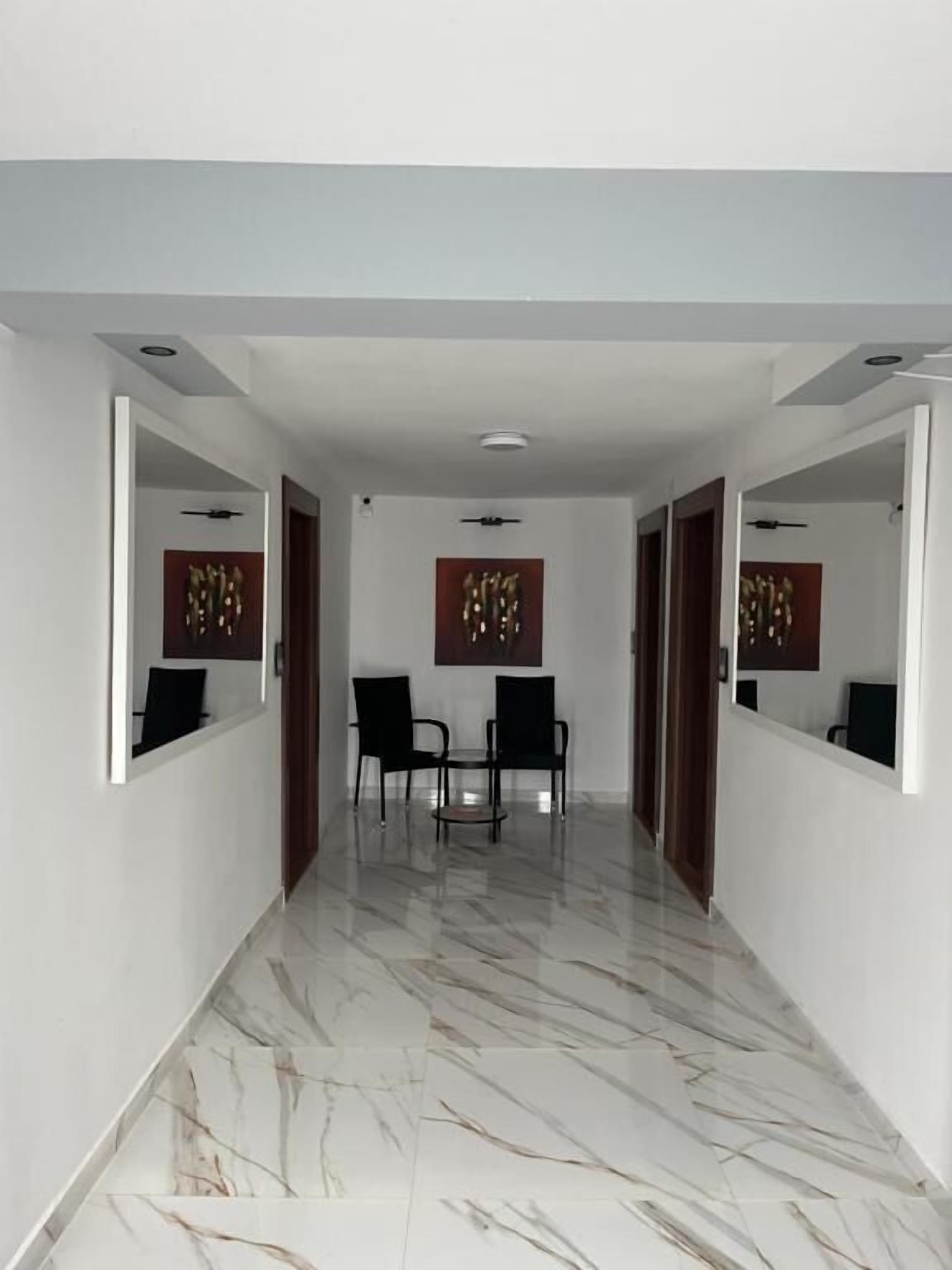 A hallway with a marble floor, two black chairs, and a small table.