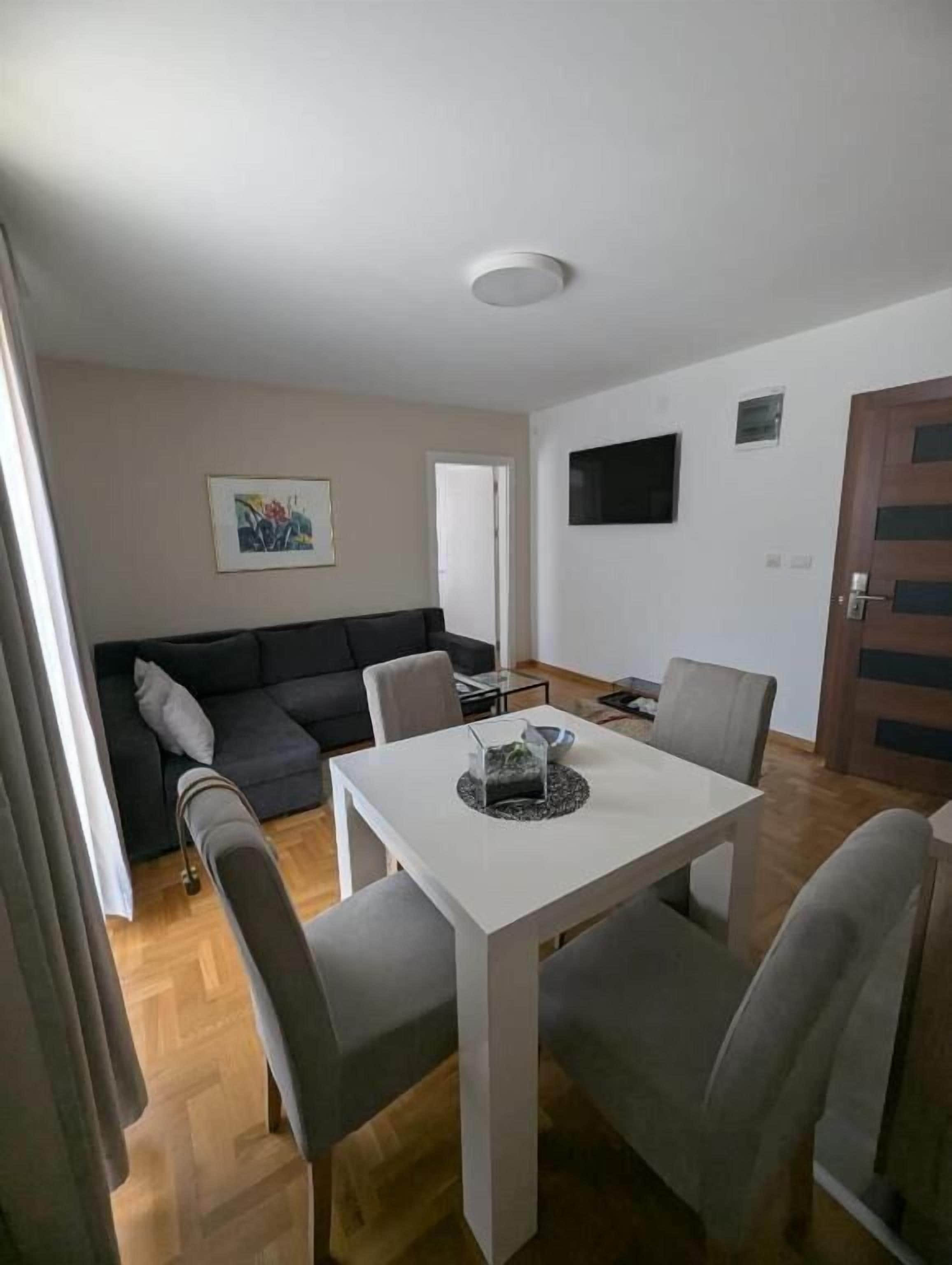 Un salon moderne comprenant un canapé, une table à manger avec des chaises, un téléviseur à écran plat fixé au mur et une porte.
