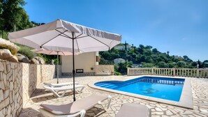 Uma piscina com espreguiçadeiras e um guarda-sol, cercada por muros de pedra e vista para o verde.