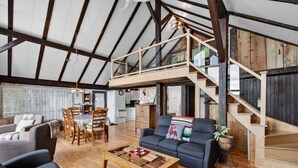Un loft spacieux avec un plafond haut, des poutres en bois, un coin repas avec des chaises et une table, un canapé et un escalier menant à un niveau supérieur.