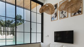 Ett modernt vardagsrum med ett stort fönster, vita soffor, en tv och flätade hänglampor.
