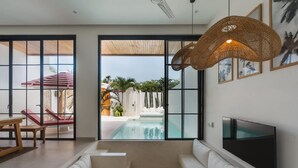 Ett modernt vardagsrum med utsikt över poolen, vita soffor, en TV och en hängande lampa i rotting.