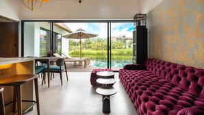 Ein modernes Interieur mit einem üppigen violetten Sofa, einem Essbereich mit Tisch und Stühlen sowie Blick auf einen Swimmingpool.