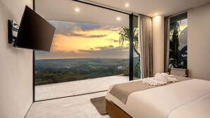 Un dormitorio moderno con una cama grande, un televisor de pantalla plana montado en la pared y un ventanal que ofrece vistas panorámicas.
