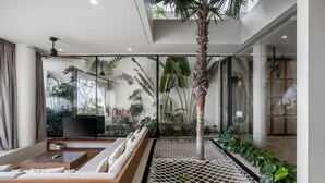 Una sala moderna con un televisor grande, un sofá de madera, una mesita de centro pequeña y una palmera decorativa.