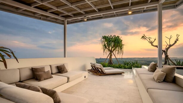 Un espacio lounge al aire libre moderno con sofá y sillones, una pérgola y vistas al paisaje.