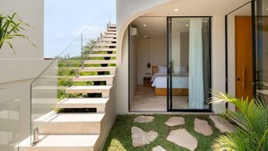 A modern interior with a staircase leading to a bedroom, a glass door, and a small outdoor area with grass and stones. - Villa Ohana in South Kuta (South Kuta)