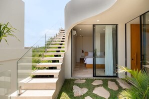 A modern interior with a staircase leading to a bedroom, a glass door, and a small outdoor area with grass and stones. - Villa Ohana in South Kuta (South Kuta)