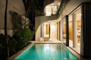 A modern poolside area with a curved building, a pool, and a seating area with cushions. - Villa Ohana in South Kuta (South Kuta)