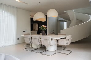 A modern dining area with a white table and chairs, pendant lighting, and a curved staircase. - Villa Sayuri in Kecamatan Kuta Utara (Kecamatan Kuta Utara)
