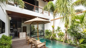 A modern outdoor pool area with a wooden deck, lounge chairs, and a glass-enclosed kitchen. - Rocca Bella Loft 1 in Canggu (Canggu)