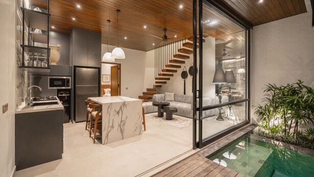 A modern kitchen with a marble island, a dining area with a sofa, and a staircase leading to a living area. - Rocca Bella Loft 1 in Canggu (Canggu)