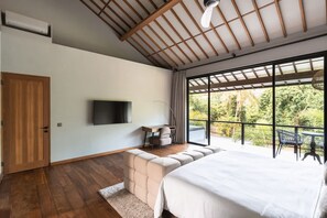 A bedroom with a large bed, a TV, a desk, and a balcony with outdoor seating. - Umayam Sanctuary in Pererenan (Pererenan)