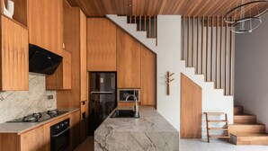 Cozinha moderna com armários de madeira, bancada de mármore, forno embutido e geladeira de aço inoxidável.