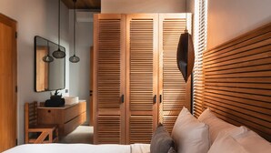 Quarto com cama, cabeceira de madeira, espelho, cômoda e armário com portas venezianas.