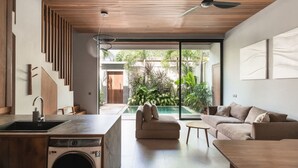 Uma cozinha moderna com máquina de lavar, área de refeições com mesa e cadeiras, sofá, e vista para uma piscina e jardim.