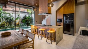 Een moderne keuken met een centraal eiland, barkrukken, een eettafel en uitzicht op een zwembad.
