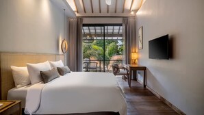 Een hotelkamer met een bed, een bureau, een televisie en een balkon met planten.