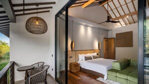 Een moderne slaapkamer met een groot bed, een groene bank, een zithoek met een tafel en stoelen, en een balkon met een balustrade.