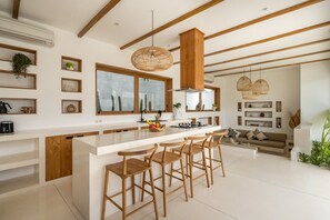 A modern kitchen with a large island, wooden bar stools, and a dining area with a sofa and plants. - Mr    Mrs  W Bingin in Kecamatan Kuta Selatan (Kecamatan Kuta Selatan)