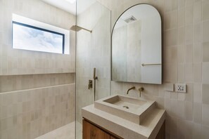 Une salle de bain moderne avec une douche à parois de verre, un grand miroir et un lavabo surmonté d’un meuble en bois.