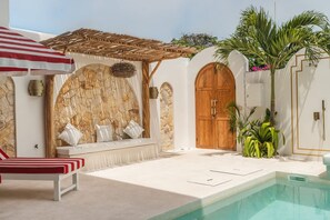 Un espace aménagé au bord de la piscine, avec un fauteuil de relaxation, une porte en bois et un mur en pierre.