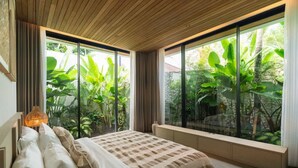 Een slaapkamer met een groot bed, een bedlampje, een raam met uitzicht op groen, en een houten plafond.