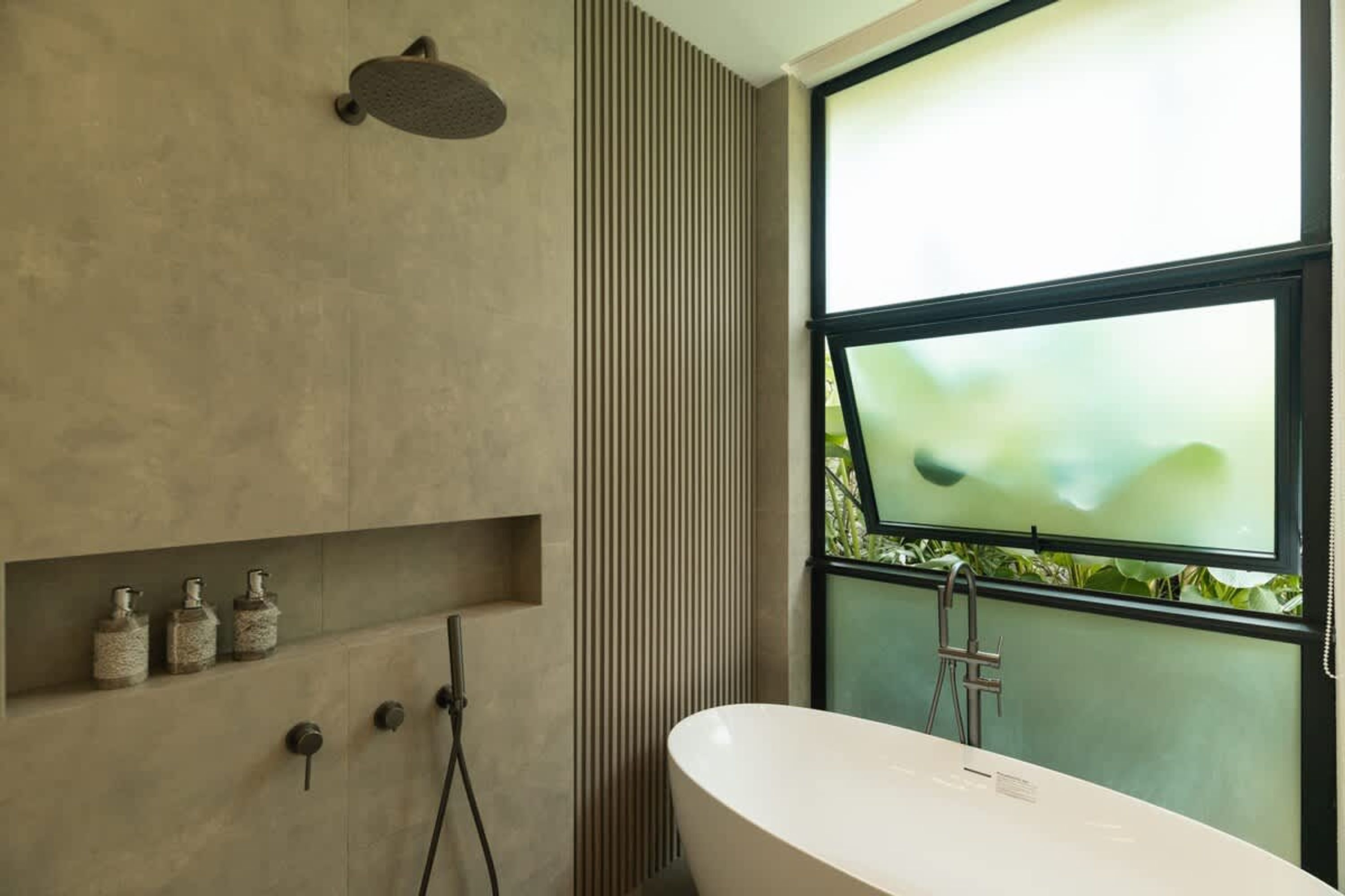 Un baño moderno con una bañera independiente, un cabezal de ducha y una ventana con vistas a la vegetación.