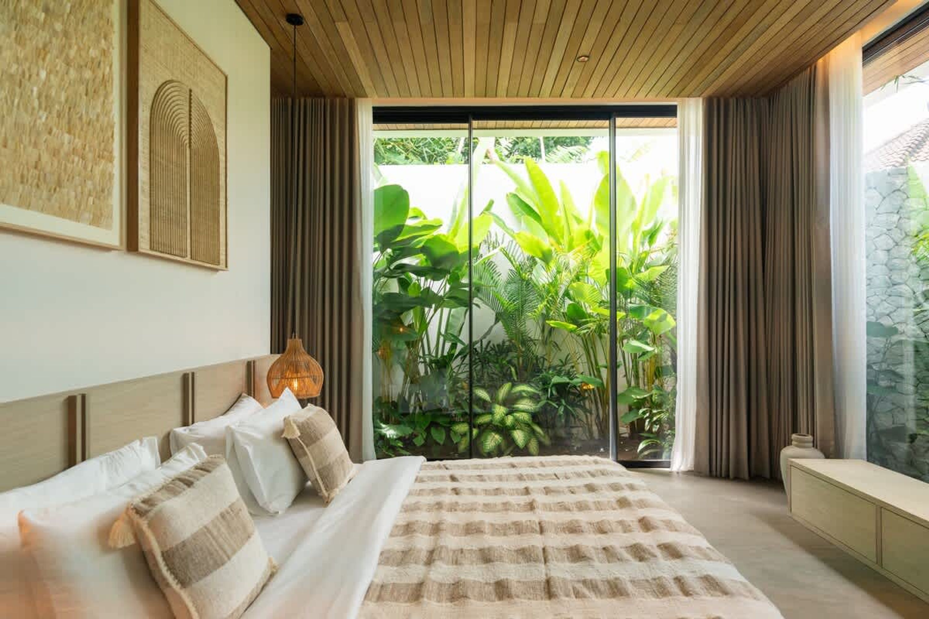 Un dormitorio con una cama grande, techo de madera y vistas a vegetación exuberante a través de una puerta de cristal.