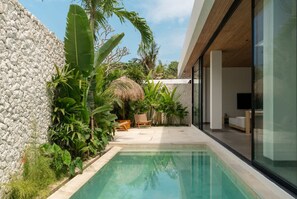 A modern pool area with a stone wall, tropical plants, and a glass-enclosed room. - Villa Moon in Pererenan (Pererenan)