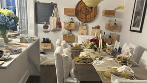 Un comedor con una mesa de madera dispuesta para una comida, sillas blancas tapizadas y una araña.