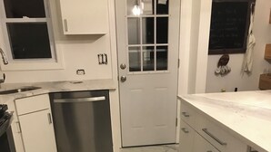Una cocina con armarios blancos, lavavajillas de acero inoxidable y suelo de mármol.