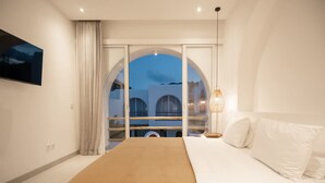 Un dormitorio con una cama grande, vistas a través de una ventana y un televisor montado.