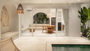Un interior moderno con una piscina, zona de comedor y sala de estar con sofá y sillones.