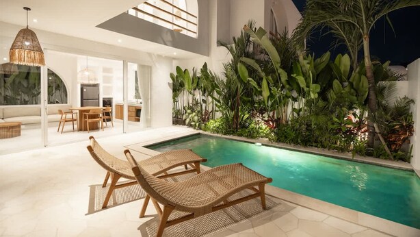 Un área de piscina interior con sillones de descanso, comedor y plantas tropicales.