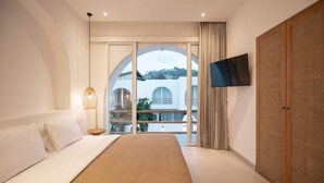 Un dormitorio con cama, televisor montado en la pared y un ventanal con vistas a edificios.